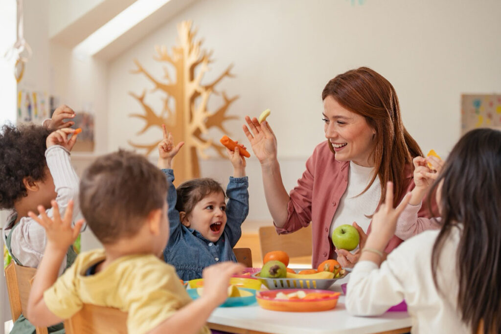 Lehrerin vermittelt Kindern spielerisch Wissen über Obst und Gemüse – Ernährungserziehung als Teil der Schulverpflegung.
