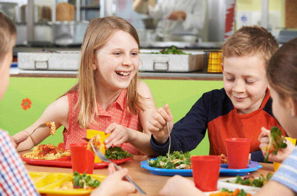 Gruppe von Grundschulkindern beim Mittagessen in der Schulcafeteria, Beitragsbild für den Blogartikel zum VDSKC
