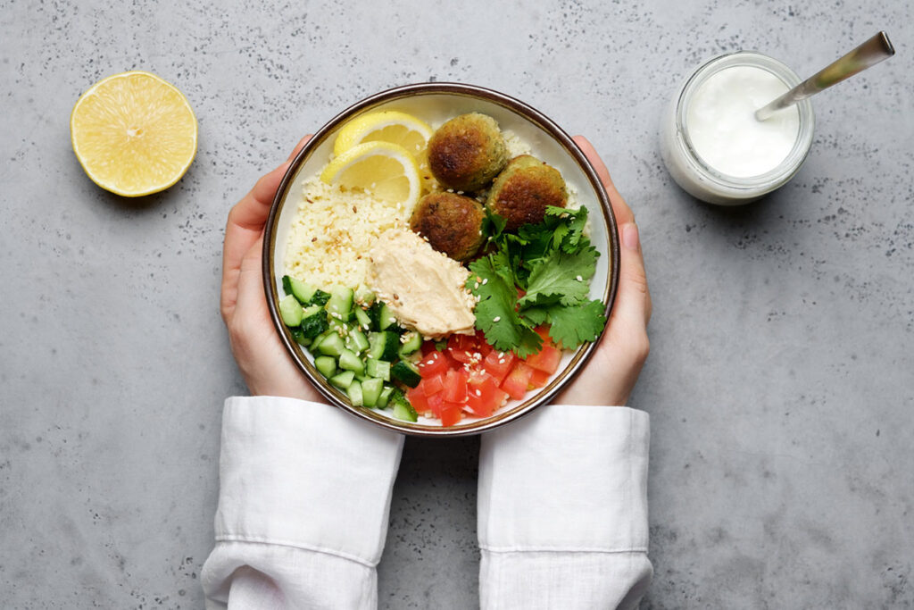 Titelbild für den Blogbeitrag Generation Alpha - Jung ist Anders, das eine Bunte gesunde Saladbowl mit Couscous, Gurke, Tomate, Falafel und Hummus.